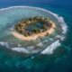 Aerial view of a small Pacific atoll with eroding coastlines and ocean waves approaching homes, symbolizing sinking islands under climate change.